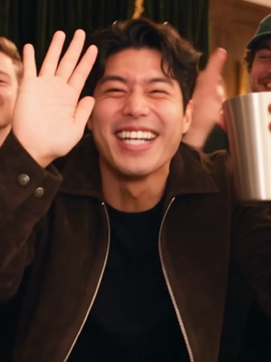 The host of a dinner party waves at the camera with a silver cup.